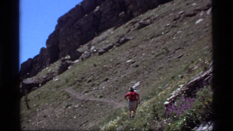 The hiker appears farther along the Sapphire Lake mountain path, moving away beneath a dark rocky ridge and clear blue sky.