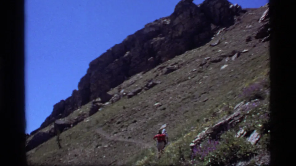 The closing frame keeps the hiker small and rear-facing on the Sapphire Lake trail, surrounded by rocks, grasses, and wildflowers.