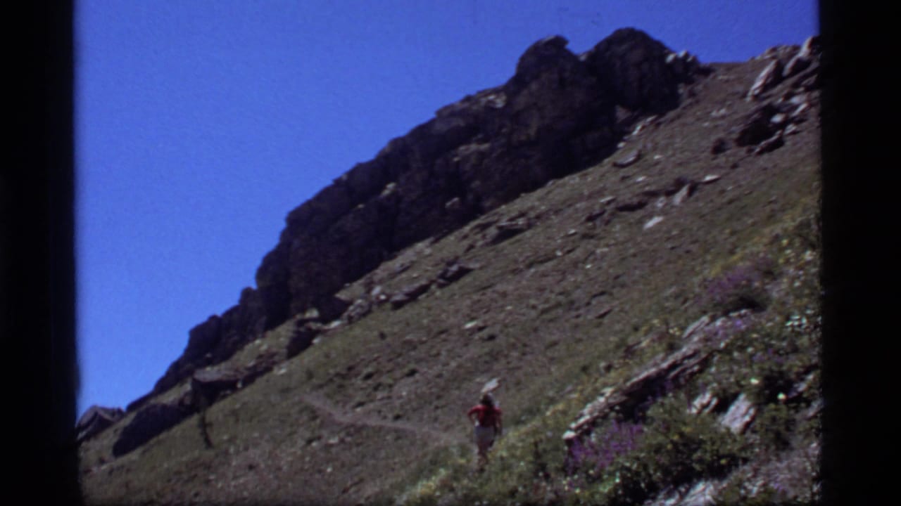 Distant hiker in red on a rocky mountain trail under a clear blue sky.