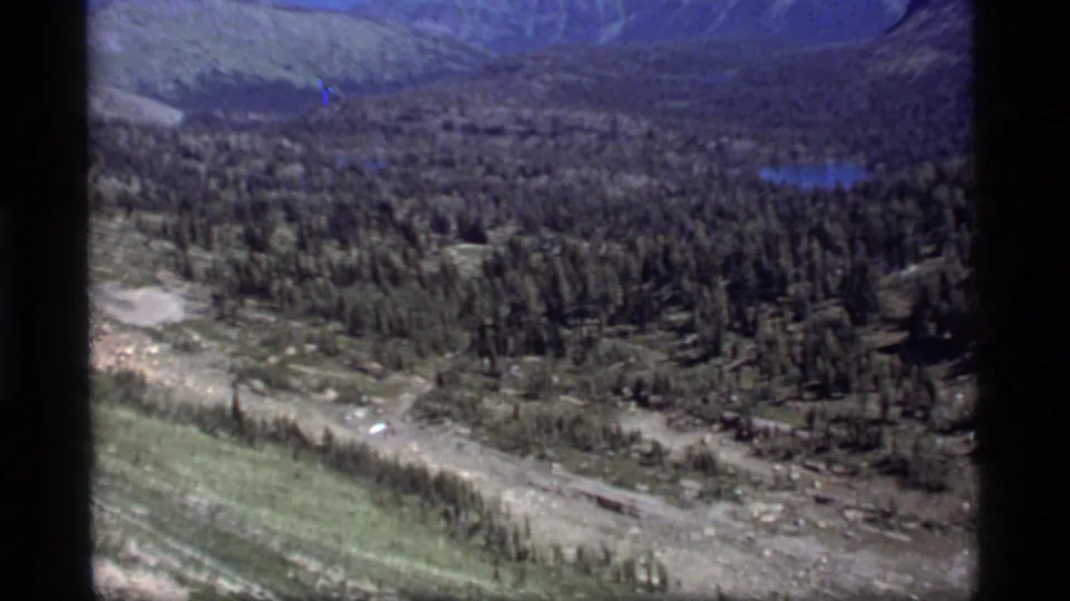 A 1977 8mm Montana landscape view shows a forested valley and distant lake near Sapphire Lake.
