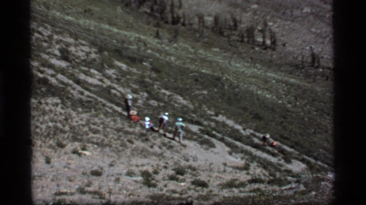 Hikers continue along a rugged hillside with scattered vegetation and exposed rock.