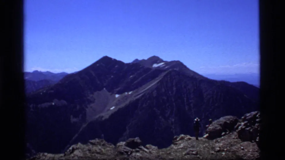 A lone hiker stands on a rocky ridge before high Montana peaks in 1977 8mm home-movie footage.