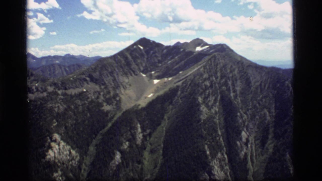 Mountain peaks and ridges viewed from above under scattered clouds.