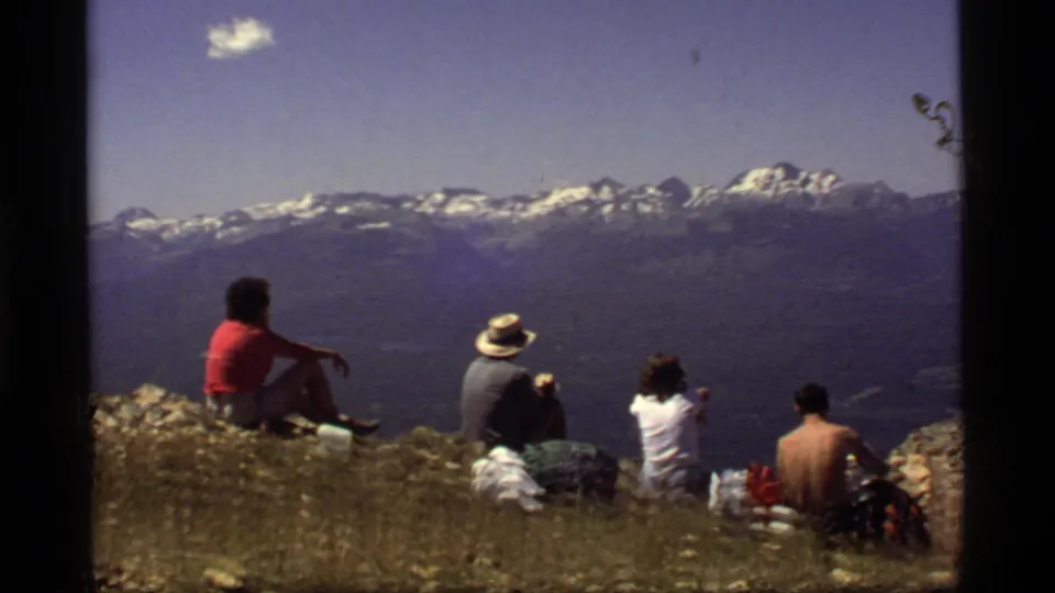 Final 1977 8mm frame shows hikers on a Montana ridge with visible film marks and smudges over the sky and mountain landscape.