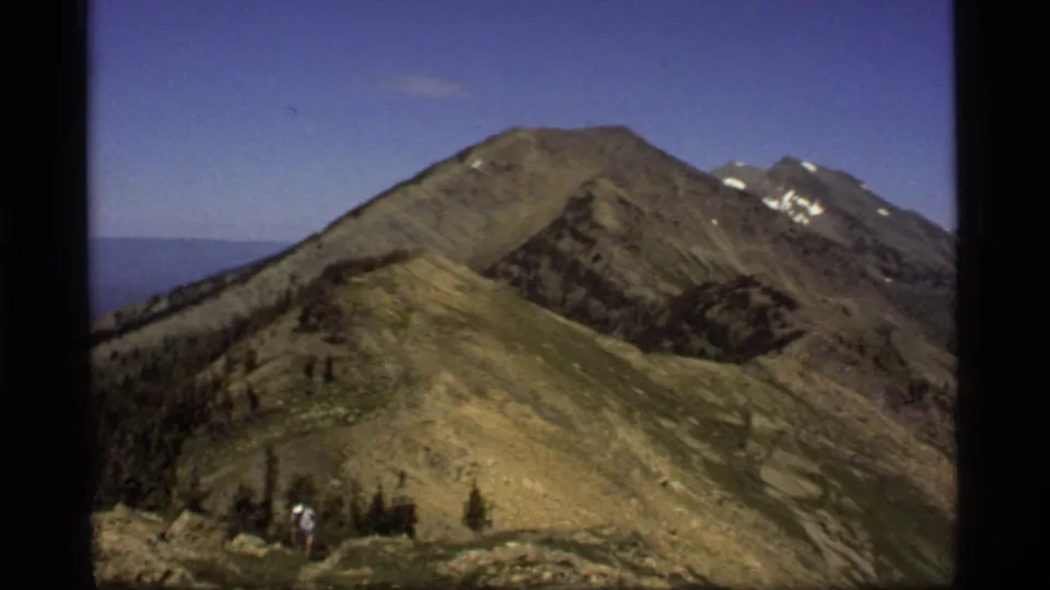 Sapphire Lake, Montana 1977 home-movie frame of a hiker crossing a rocky ridge under a clear blue mountain sky.