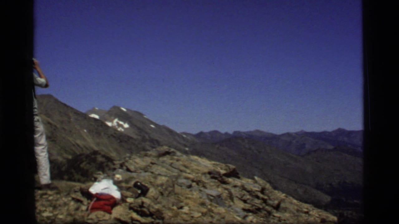 Rocky mountain overlook with part of a man at left and distant ridges beyond.