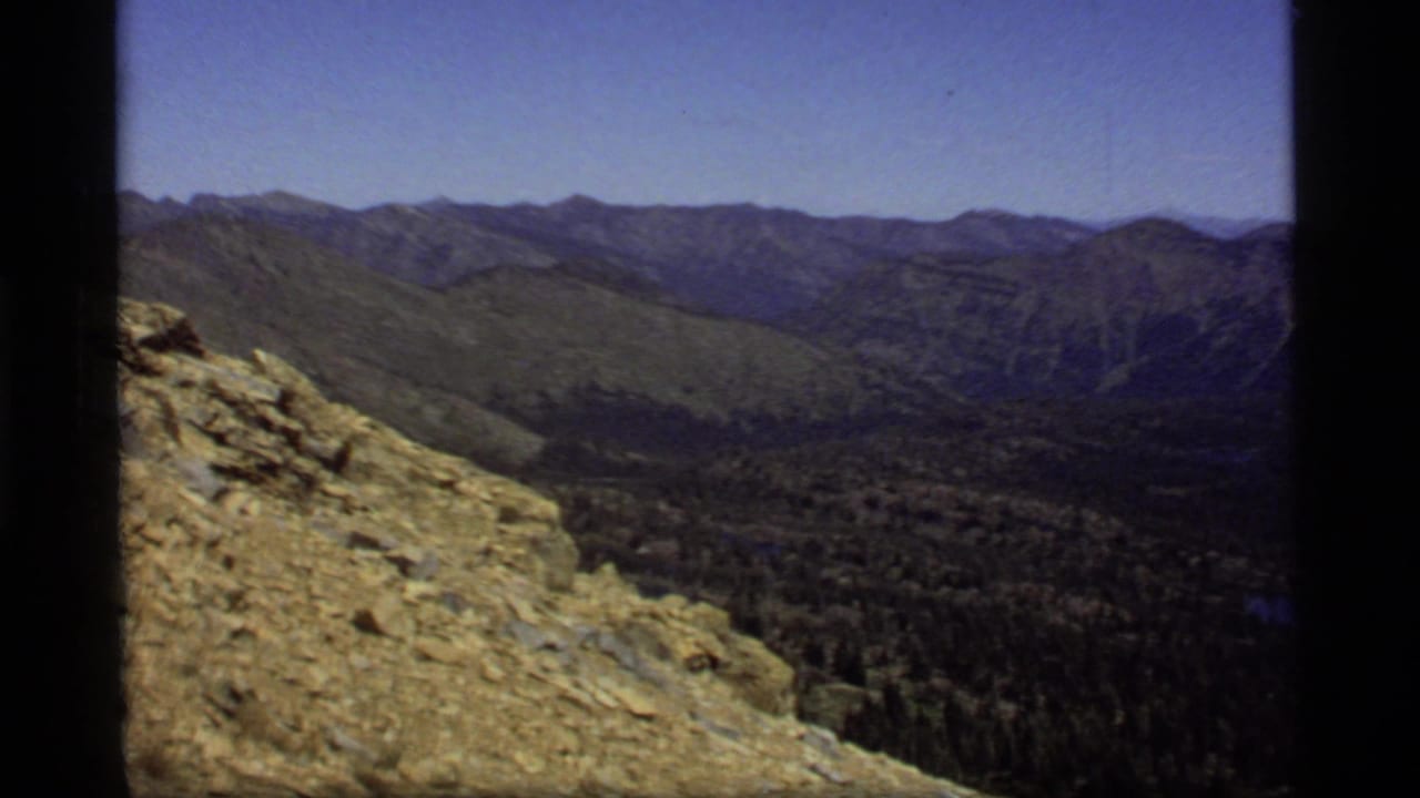Vintage 8mm panorama at Sapphire Lake, Montana, showing a rocky high slope above forest and distant ridges.