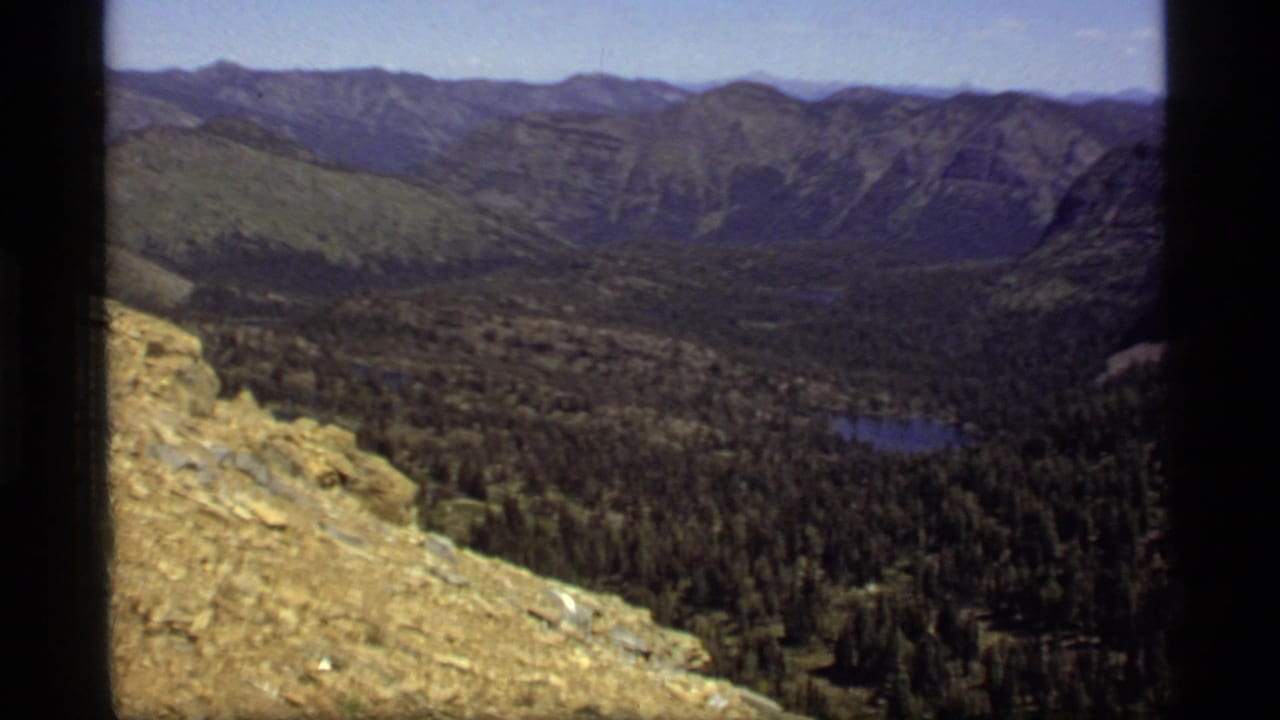 1977 8mm view of Sapphire Lake, Montana, showing a rocky overlook above forested valley, ridges, and a small blue lake.
