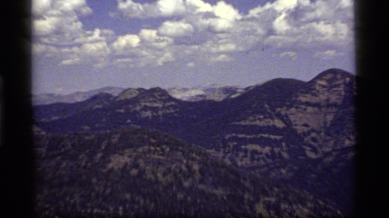 Broad mountain panorama with ridges, valleys, clouds, and visible film gate borders.