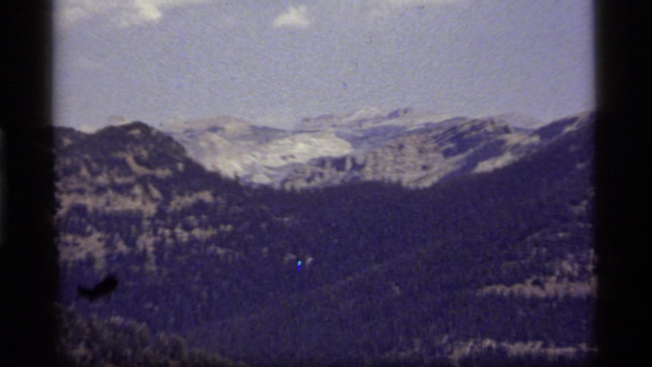 Distant mountain ridge and forested slopes under a pale sky with dark 8mm frame borders.