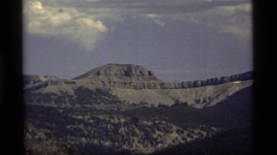 Final 1977 Montana 8mm frame with a rounded ridge, dark wooded slopes, thin clouds, and visible home-movie grain.