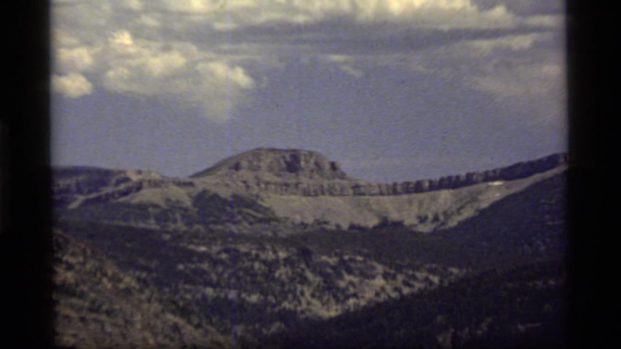Distant mountain range with rocky slopes, darker foreground hills, and a bright clouded sky.