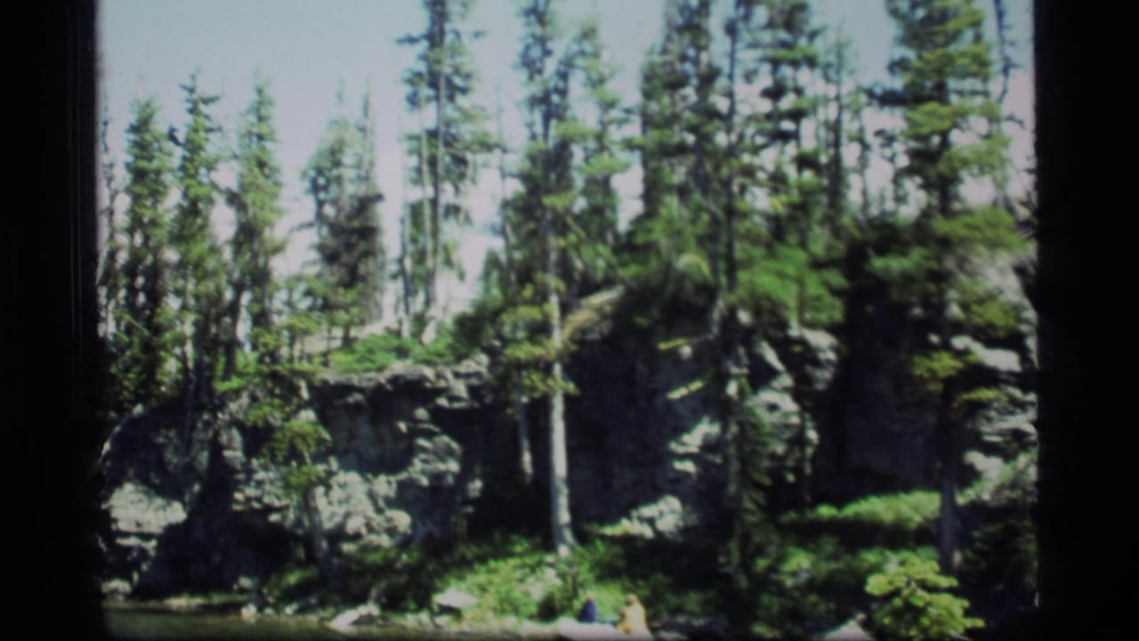 1977 Sapphire Lake, Montana home-movie frame showing evergreen trees, gray boulders, and a rocky forest landscape.