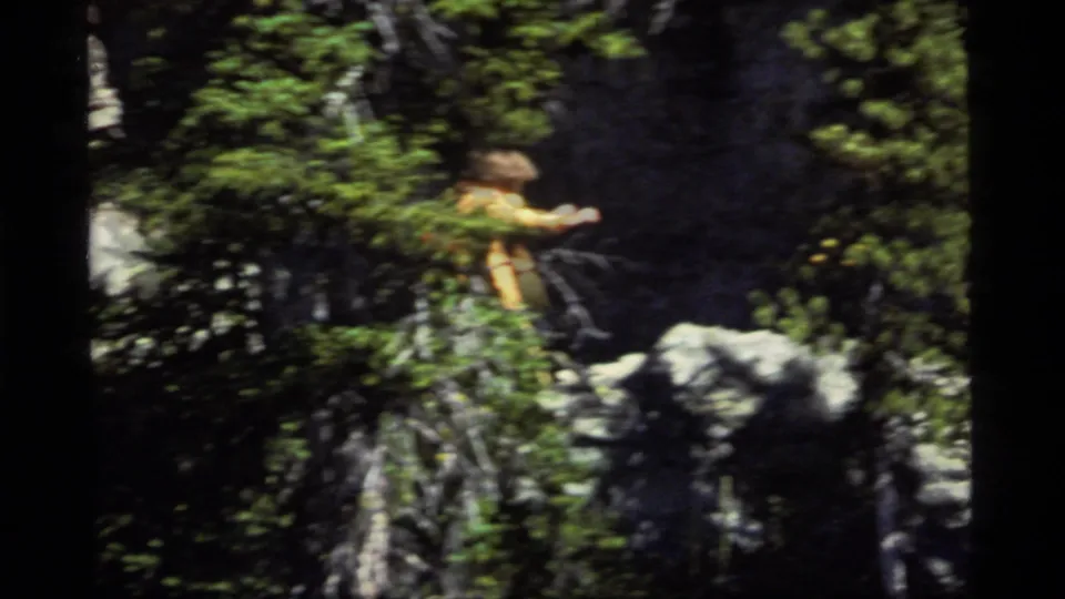 A distant hiker in an orange jacket appears on a rocky forest trail at Sapphire Lake, Montana, in 1977 8mm footage.