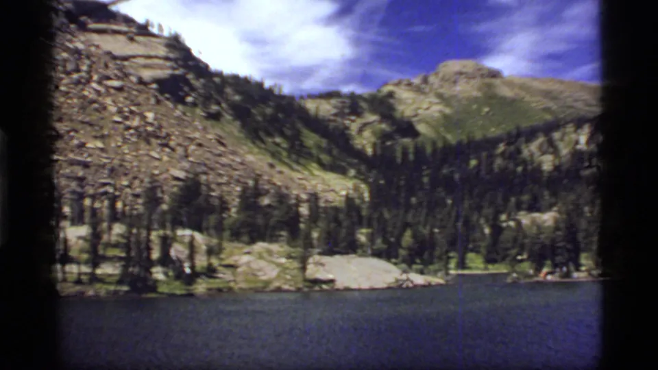 Final 1977 Sapphire Lake, Montana frame showing a wide lake foreground, conifer shoreline, rocky slopes, and distant peak.