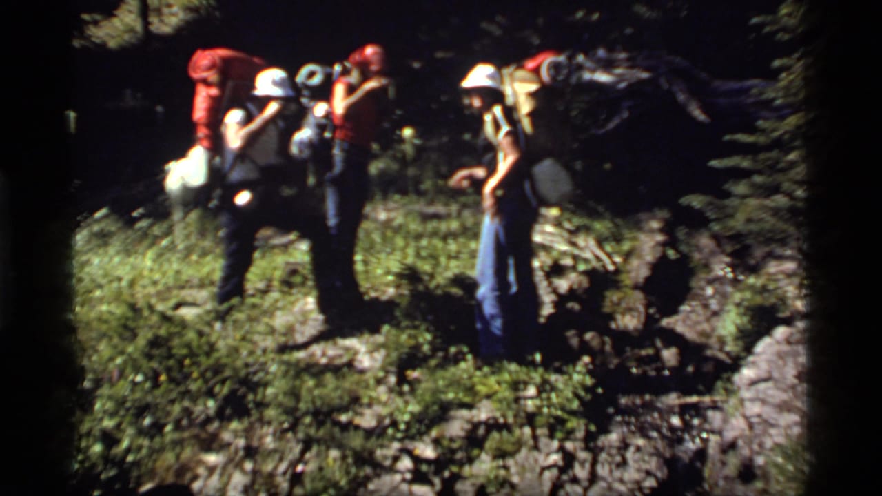 Hikers with large packs stand and adjust gear on a wooded trail at Sapphire Lake, Montana, in 1977.