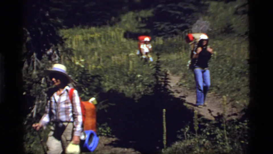 A 1977 8mm frame shows backpackers on a Sapphire Lake trail, with dense forest vegetation around the path.