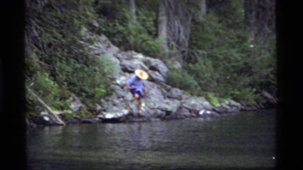 Man bends forward while stepping across rocks near the waterline.