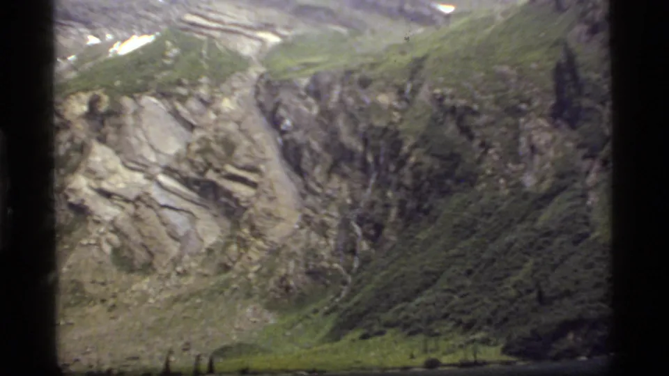 A broad view of rocky slopes and green terrain above the lake at Sapphire Lake, Montana, in 1977 home-movie footage.