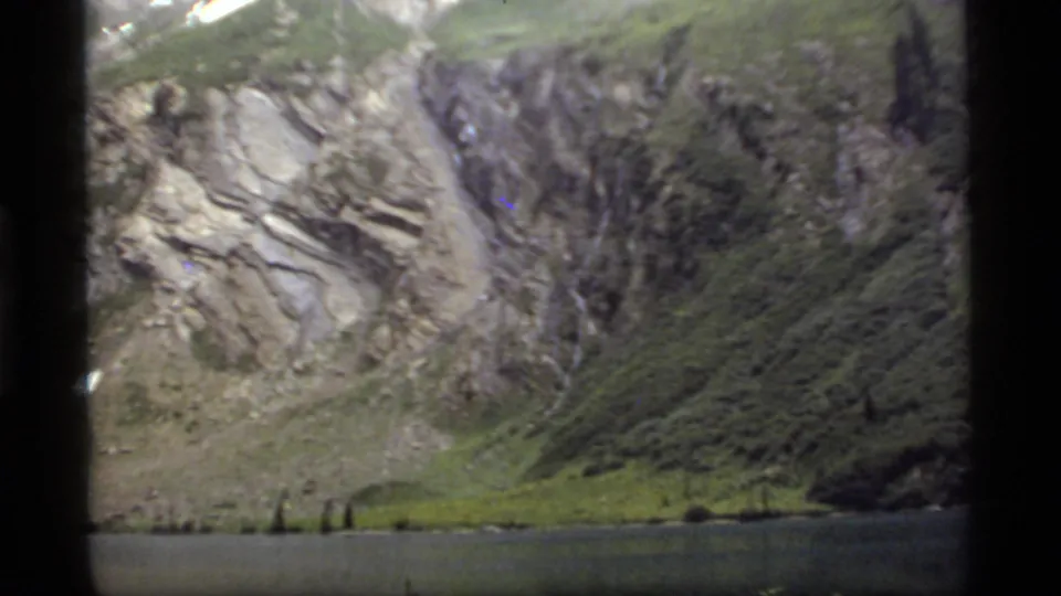 Sapphire Lake sits below steep rocky slopes and a small waterfall in soft 1977 8mm footage from Montana.