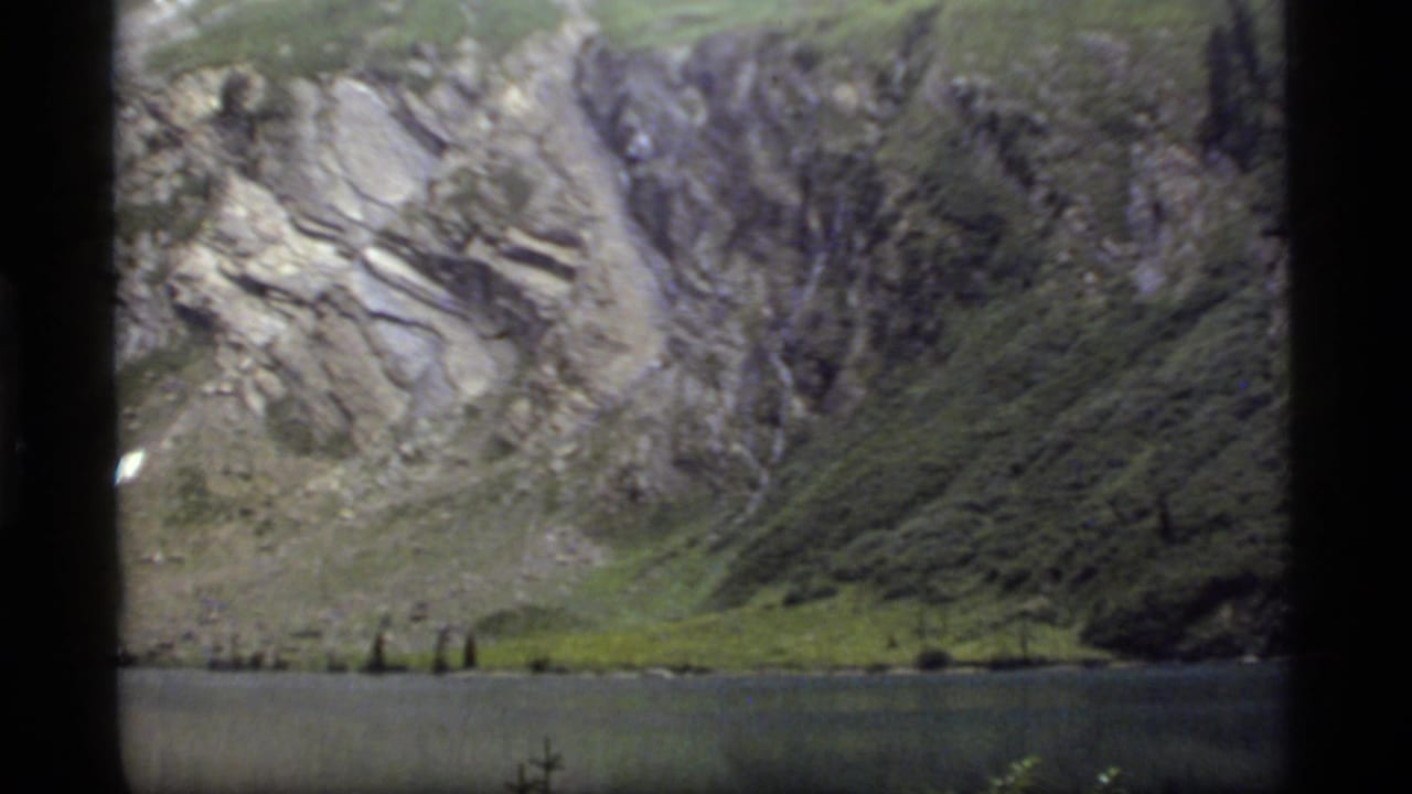 Mountain lake below steep rocky slopes with evergreen trees near the shore.
