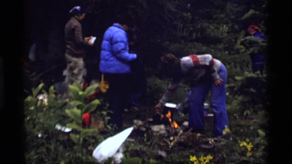 1977 Montana campsite scene with several campers in outdoor clothing gathered near a small fire in the woods.