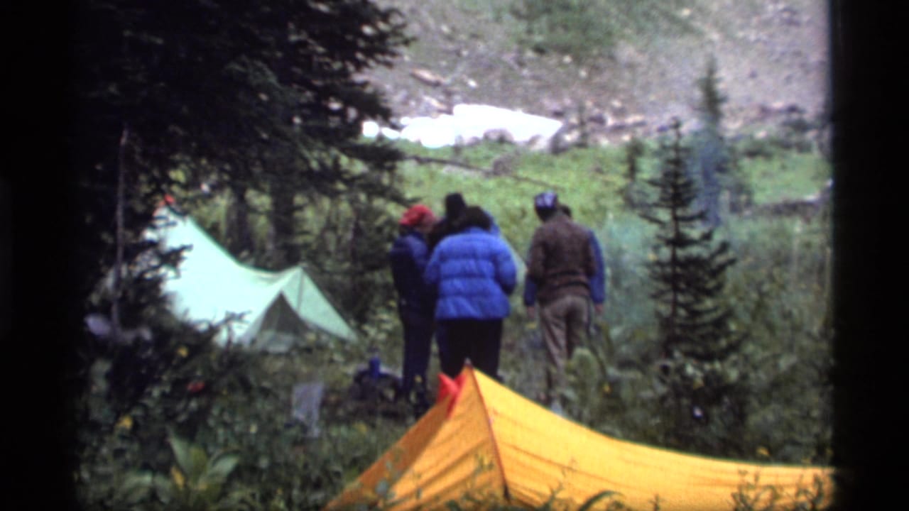Campers gather by colorful tents in a Sapphire Lake mountain valley with evergreens, rocky slopes, and snow patches.