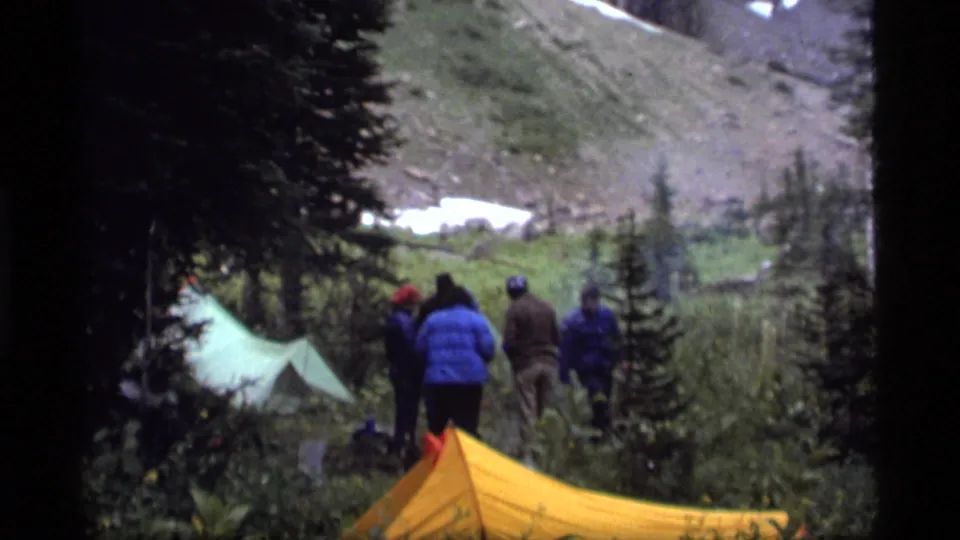 Several campers stand with their backs to the camera beside tents in the 1977 Sapphire Lake mountain campsite scene.