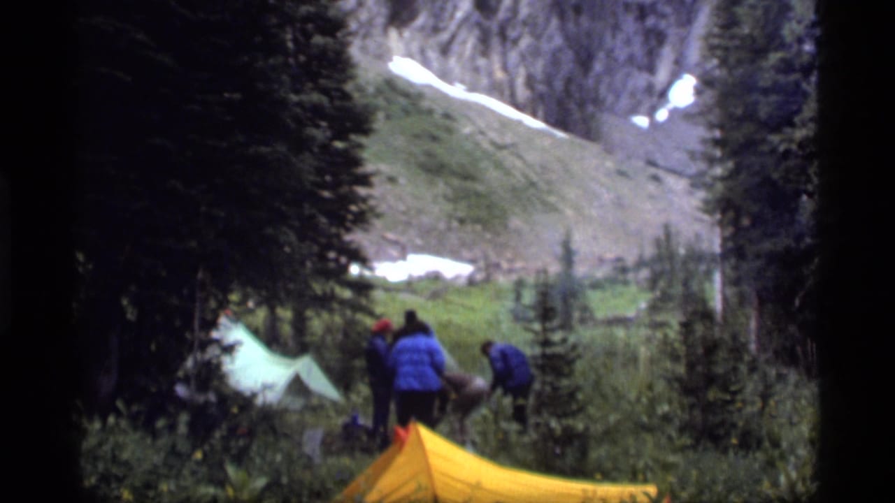 1977 8mm home-movie frame at Sapphire Lake, Montana, showing campers near tents in a wooded mountain clearing.