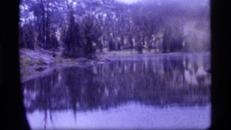 Sapphire Lake, Montana, in 1977, with a wooded shoreline and hill reflections on calm water in soft 8mm color.