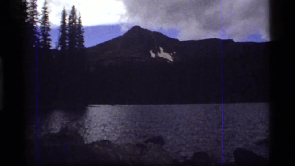 Sapphire Lake view with dark mountain slopes, lakeside trees, reflective water, and a soft 8mm exposure shift.