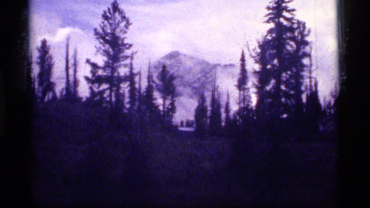 1977 8mm view at Sapphire Lake, Montana, with a misted mountain peak framed by dark evergreen silhouettes.