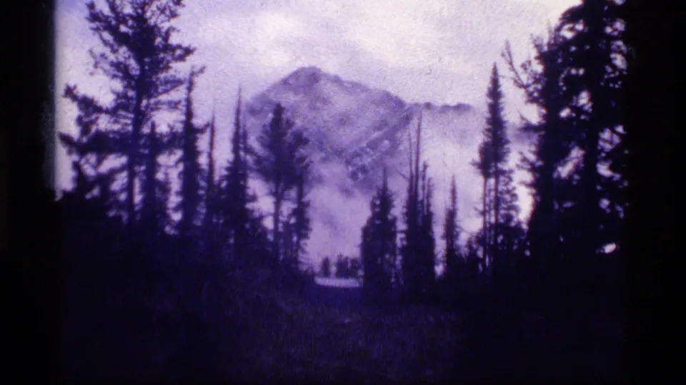 Final 1977 Sapphire Lake view with a distant mountain peak, mist, and dark evergreen trees filling the foreground.