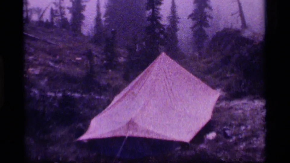 1977 Sapphire Lake, Montana frame showing a red tent against a misty evergreen forest backdrop.
