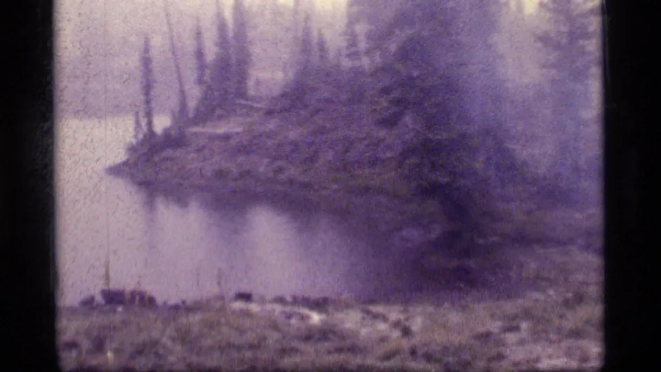 A misty lakeside view at Sapphire Lake, Montana, showing evergreen shoreline, water, rocky ground, and faded 8mm texture.