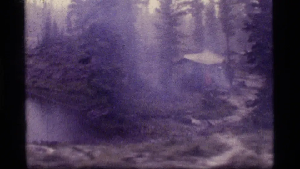 A purple-tinted 8mm frame shows the Sapphire Lake campsite, with a tent near the right edge and wet forest around it.