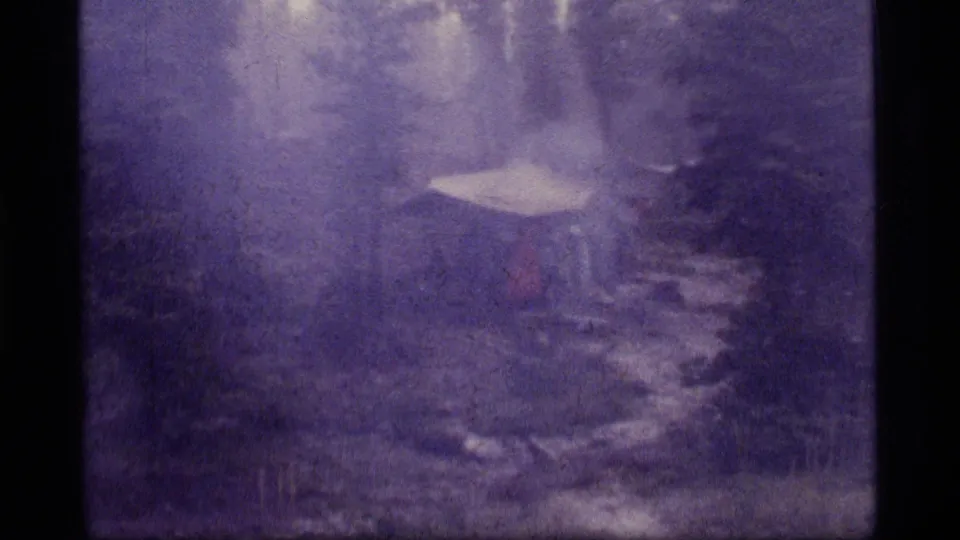 Soft 8mm frame of the Sapphire Lake campsite, with the tent more centered among conifers, rocks, and damp ground.