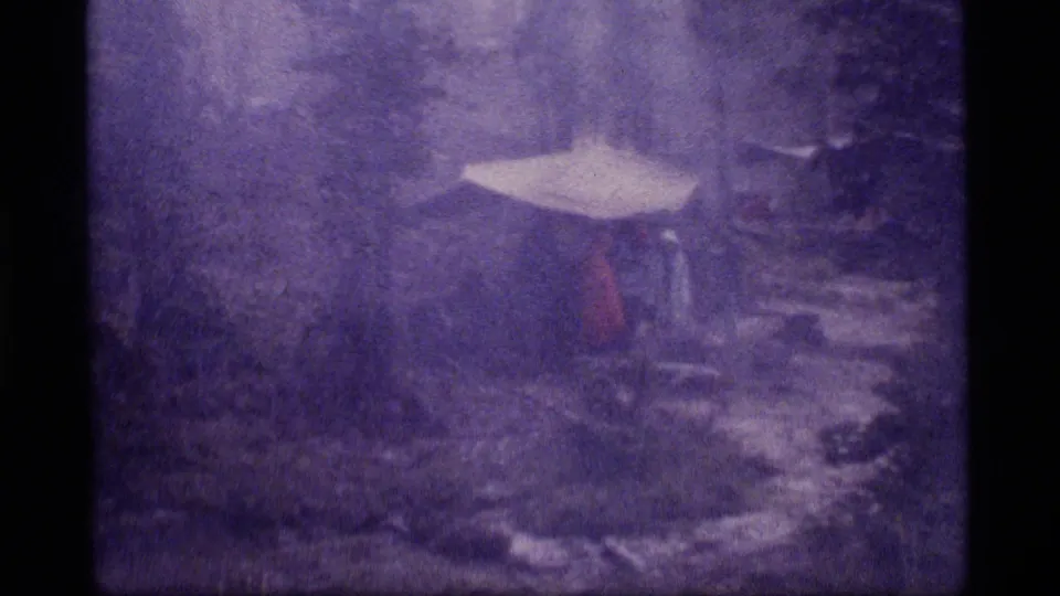 Sapphire Lake winter campsite in 1977 home-movie footage, with a pale tarp or tent visible through snow, haze, and dense trees.