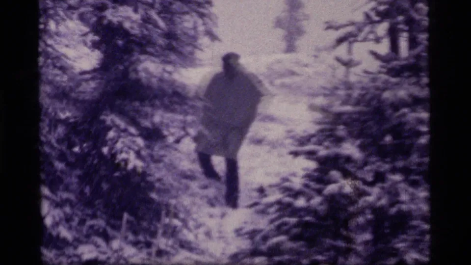 A bundled person walks through the snowy Sapphire Lake forest in this 1977 8mm home-movie frame.