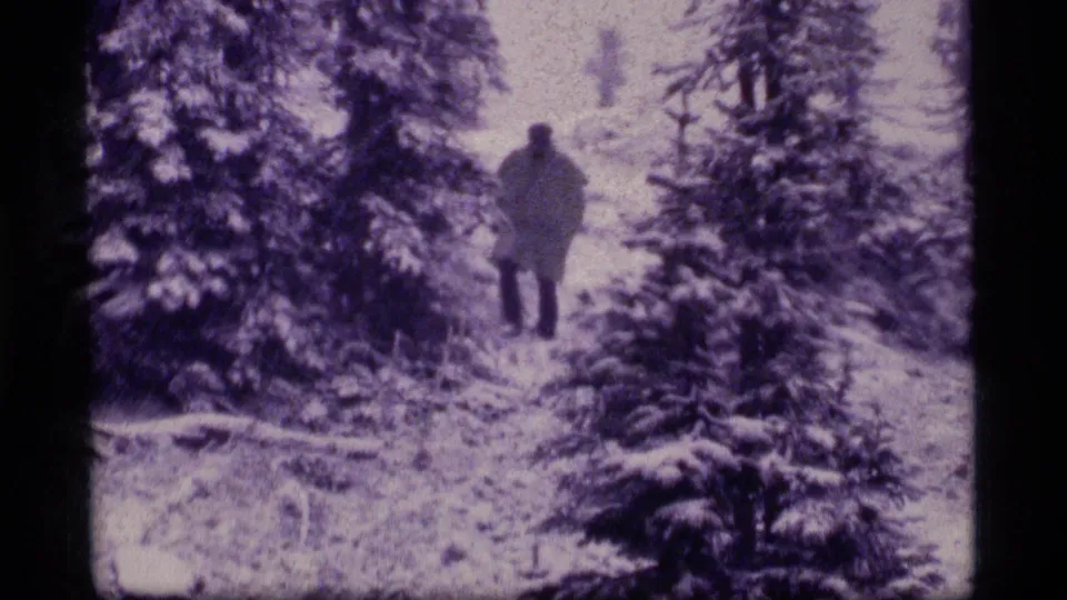 A lone bundled figure moves through snow-covered evergreens at Sapphire Lake, Montana, in 1977 8mm footage.