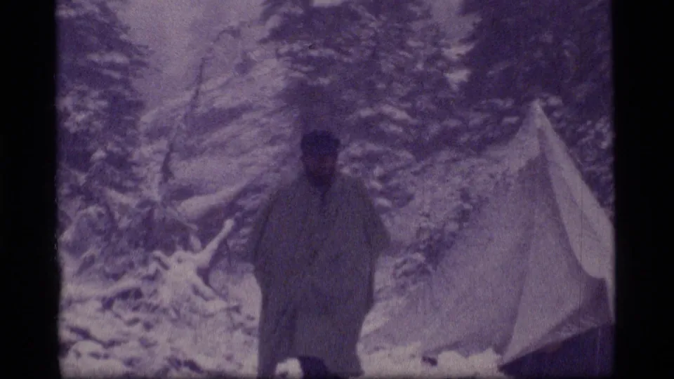 1977 Sapphire Lake, Montana 8mm frame showing a lone camper near a small tent among snow-covered evergreens.