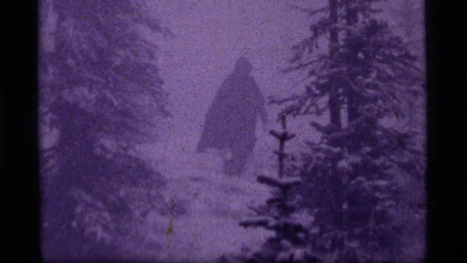 1977 Sapphire Lake, Montana 8mm frame showing a lone camper receding into a snowy evergreen landscape.