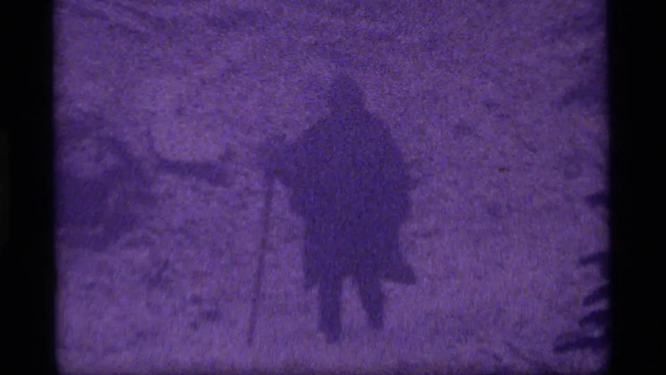 1977 Sapphire Lake 8mm frame showing a hooded person walking through snow with a shovel-like tool in a wooded area.