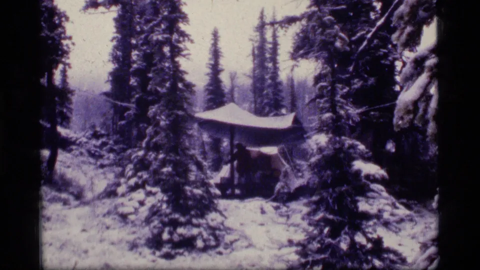 Home-movie view of a snow-covered Montana campsite, with a tarp roof and surrounding evergreen trees.