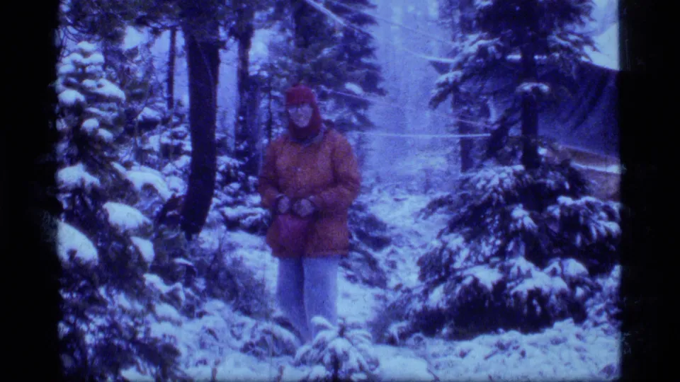 Closer 1977 Sapphire Lake, Montana home-movie frame of a man in a red coat facing the camera in snow-covered woods.