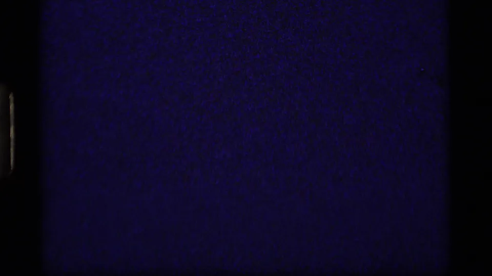 A 1977 8mm contact frame from Sapphire Lake shows a dark exposed strip beside rock, grass, and lakeside underbrush.