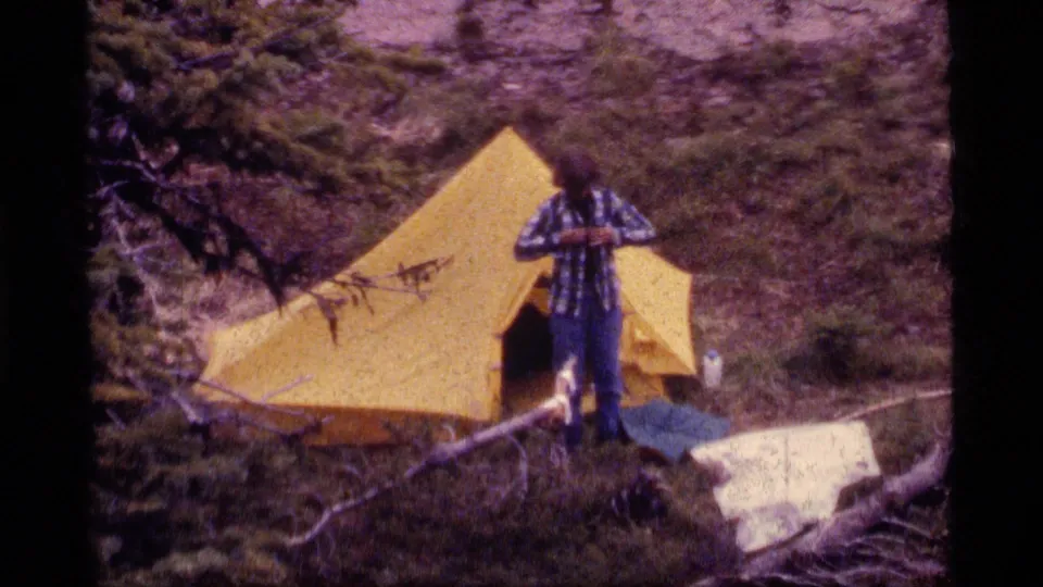 A 1977 Sapphire Lake camping frame shows the camper near the yellow tent, with forest floor, logs, and gear visible.