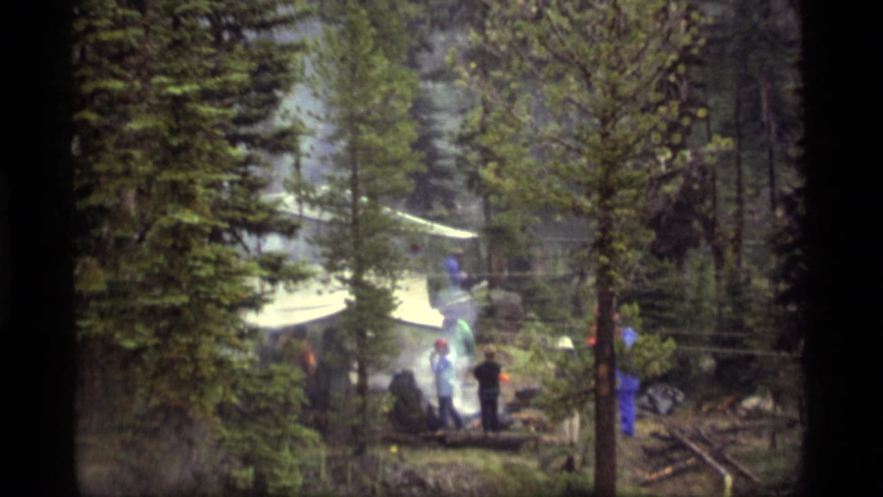 1977 Sapphire Lake, Montana 8mm frame showing distant people gathered by a smoky forest campsite under a white canopy.