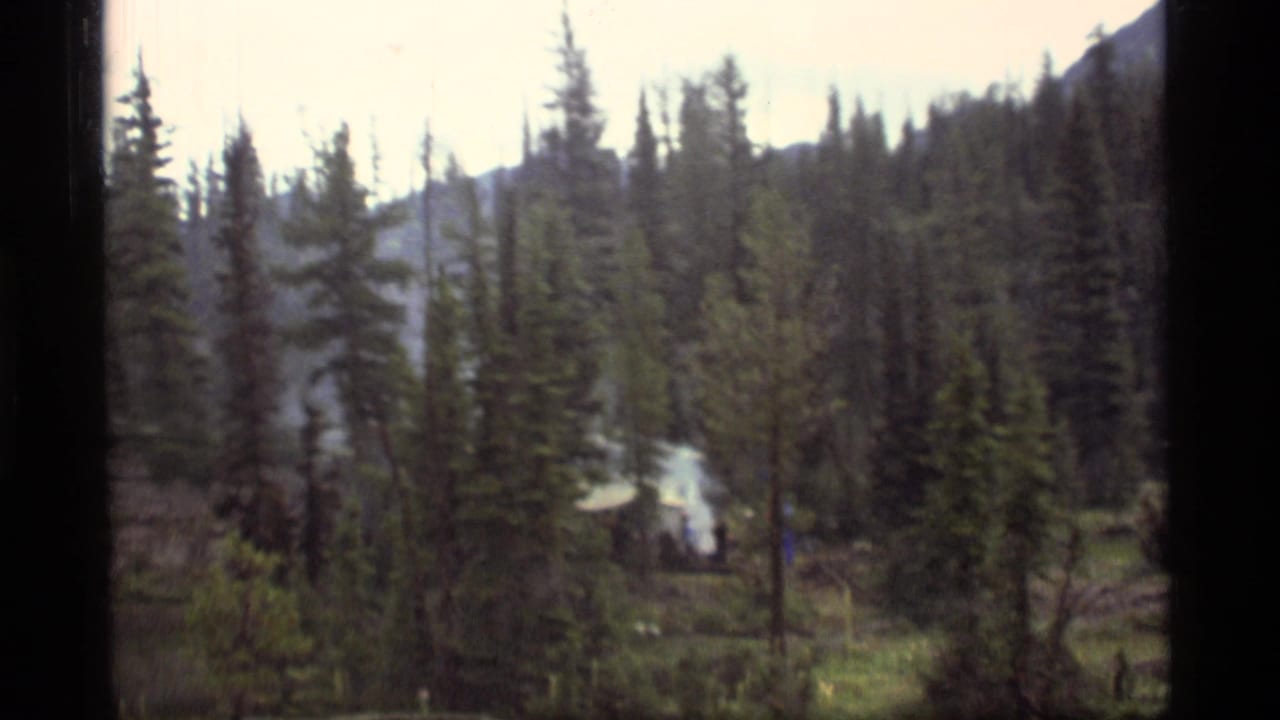 1977 Sapphire Lake, Montana 8mm frame showing evergreens, mountain slope, and smoke rising from a small camp structure.
