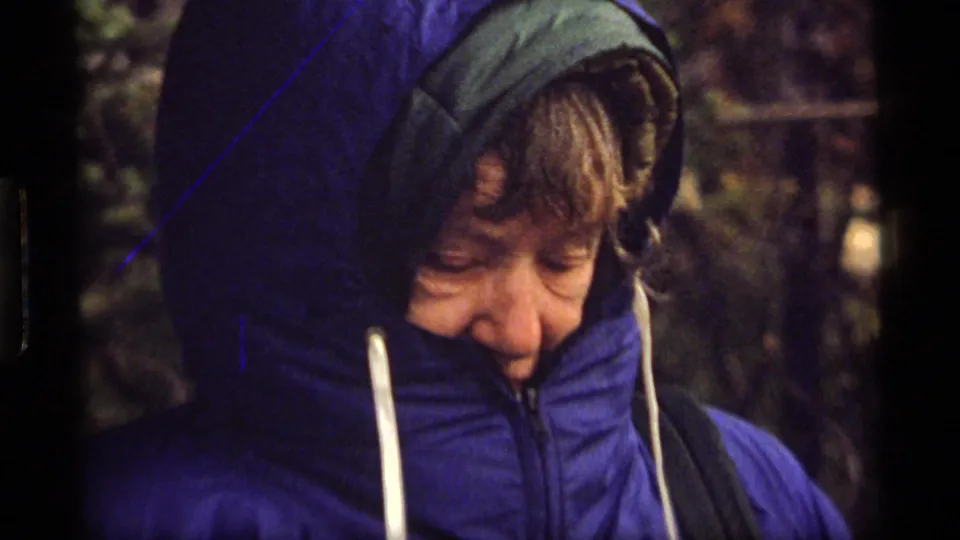 Close 8mm frame of an older person in a blue hooded jacket looking downward outdoors at Sapphire Lake, Montana.